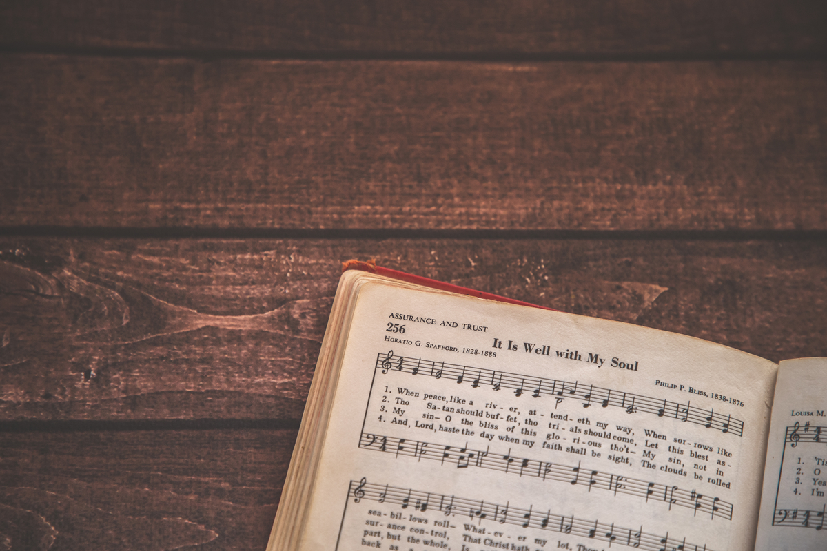 A close-up of an open hymn book displaying the lyrics to 'It Is Well with My Soul' by Horatio G. Spafford on a wooden surface.