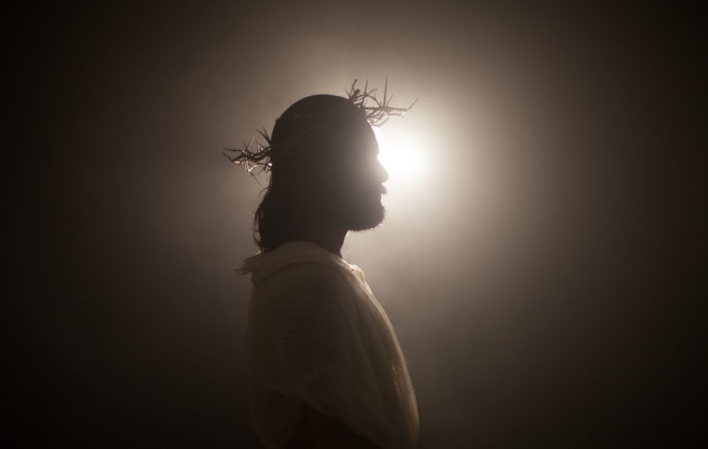 Silhouette of a man wearing a crown of thorns against a bright backlight, creating a dramatic and spiritual atmosphere.