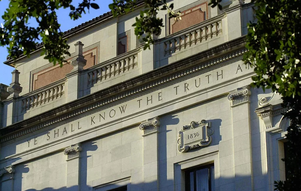 Close-up view of a historic building's upper facade featuring the engraved phrase 'YE SHALL KNOW THE TRUTH AND' and the year '1836', surrounded by decorative architectural elements.